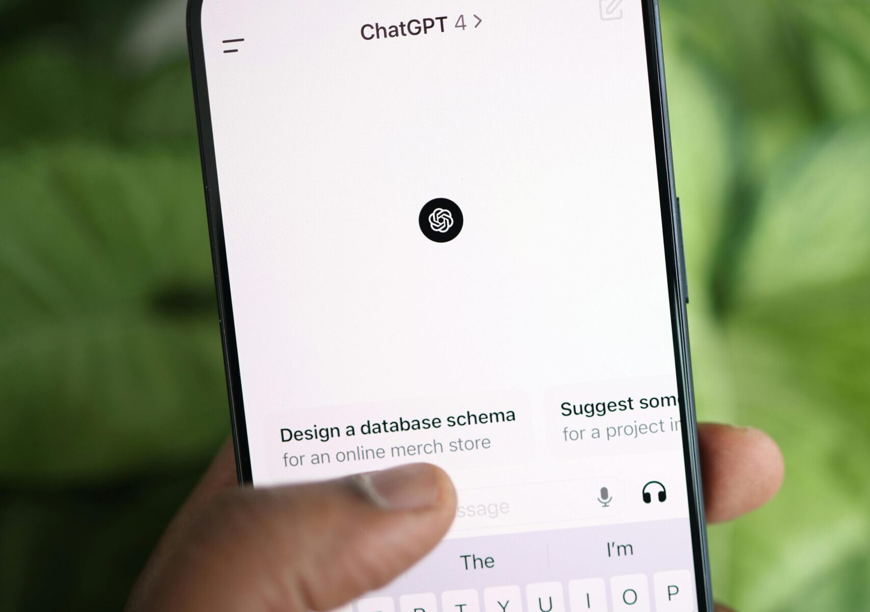 Hand holding smartphone displaying ChatGPT interface, surrounded by greenery.