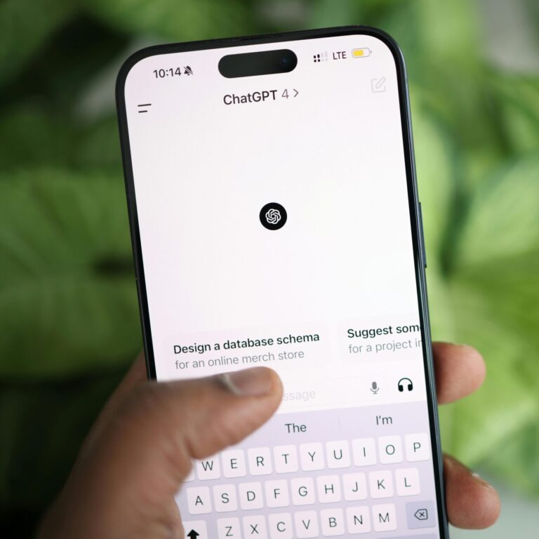 Hand holding smartphone displaying ChatGPT interface, surrounded by greenery.